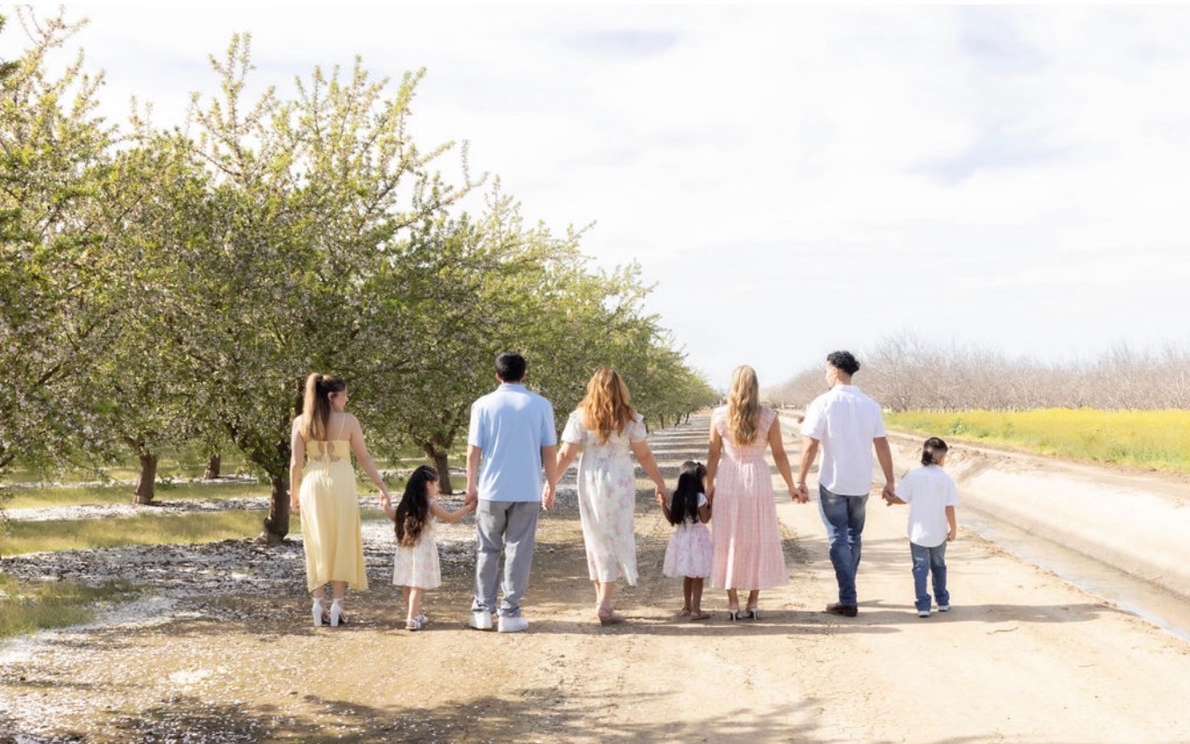 The Belita Bee family walking together through a blossoming orchard